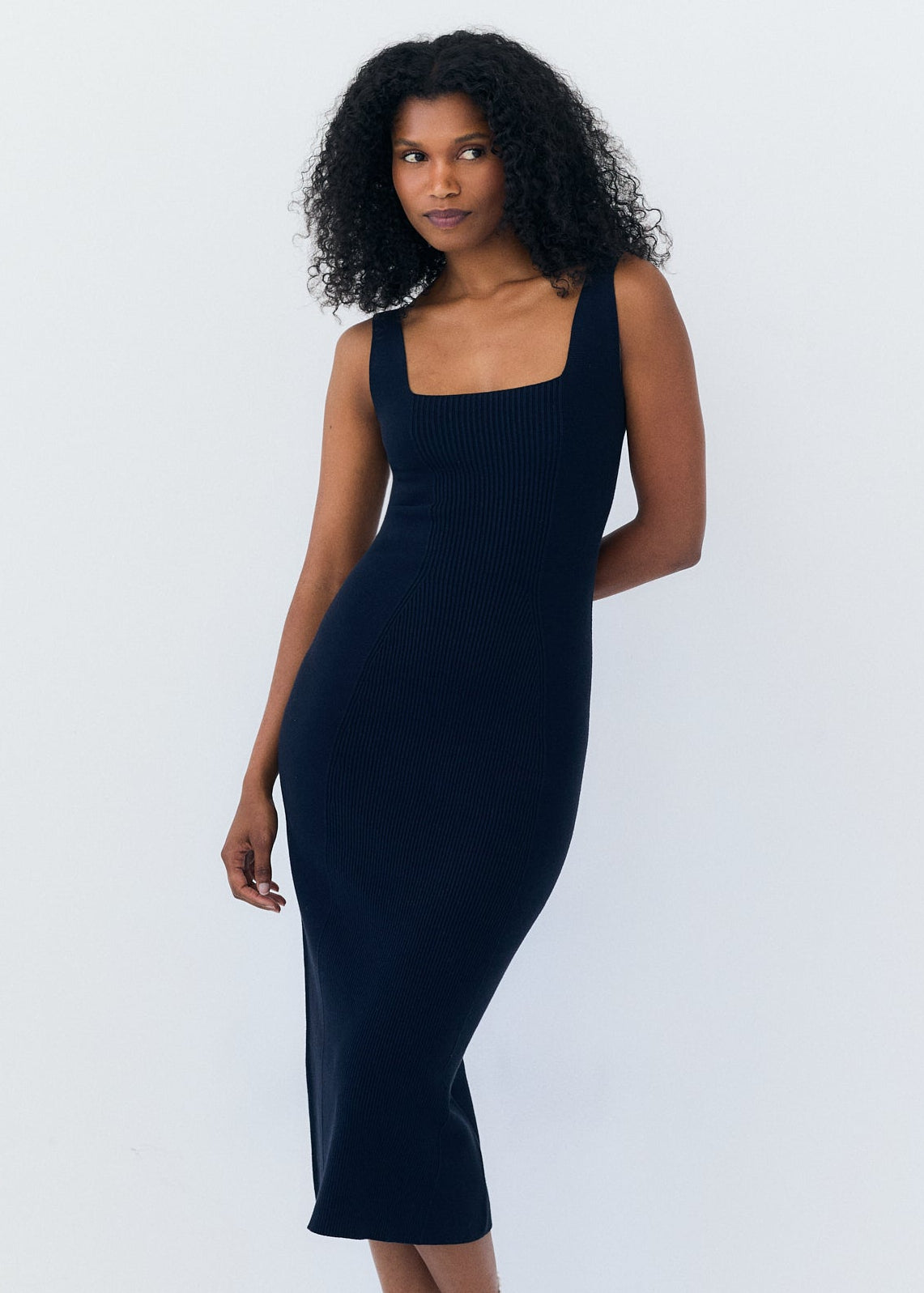 A woman modeling a sleeveless, bodycon midi dress in navy against a plain white studio background.